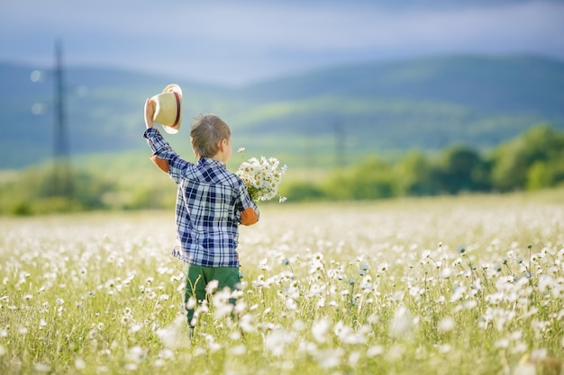 Ein kleiner Junge steht auf einem Grasfeld und schwenkt den Hut über den Kopf