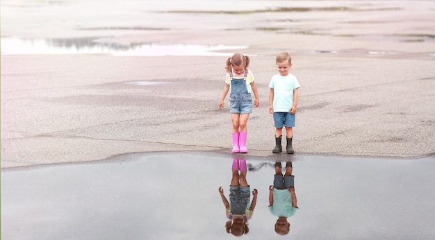 Ein kleiner Junge und ein Mädchen in Gummistiefeln stehen nach dem Regen nachdenklich in der Nähe einer Pfütze