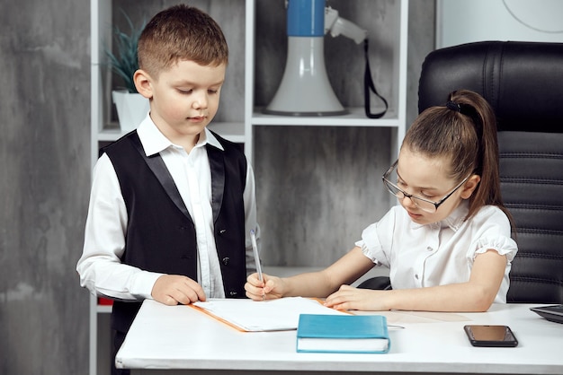 Ein kleiner Junge und ein Mädchen porträtieren Büroangestellte, eine Chefin und einen Assistentenjungen