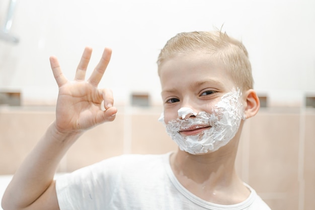 Ein kleiner Junge versucht zum ersten Mal, sein Gesicht zu rasieren Kind mit Rasierschaum