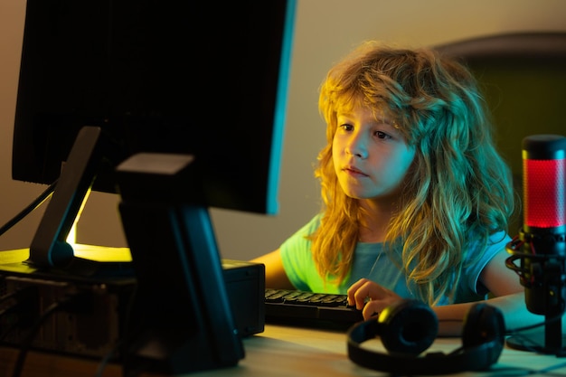 Ein kleiner Junge verwendet nachts einen Desktop Ein Kind mit Computerbildschirm im Raum mit Neonblitzen Schulstudie Online-Lernkonzept Schuljunge, der auf der Tastatur tippt