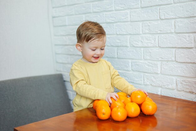 Ein kleiner Junge von 2 Jahren steht an einem Tisch mit Mandarinen. Baby möchte sich zum ersten Mal auf Zitrusfrüchte setzen