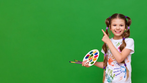 Ein kleiner Künstler mit einer Farbpalette weist auf Ihre Werbung auf einem grün isolierten Hintergrund hin Kunstkurse für Kinder
