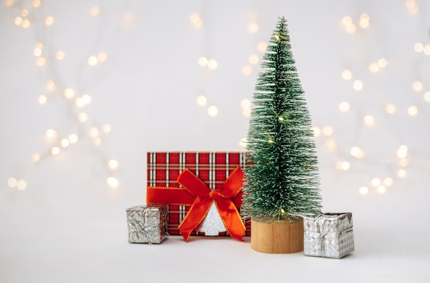 Ein kleiner künstlicher Weihnachtsbaum mit Neujahrsgeschenken auf weißem Hintergrund mit einem Bokeh mit Platz für Text