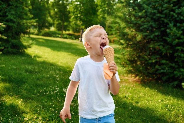 Ein kleiner rothaariger fünfjähriger Junge isst leckeres cremiges Eis in einer Waffeltüte im Park