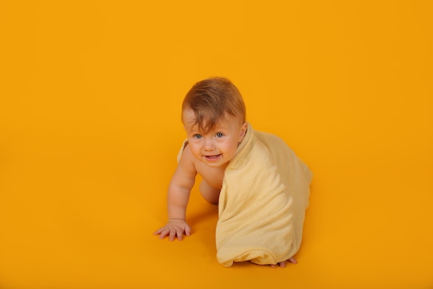 Ein kleiner schöner Junge mit Blau, der mit einem Handtuch bedeckt ist, kriecht auf einem gelben Hintergrundstudio