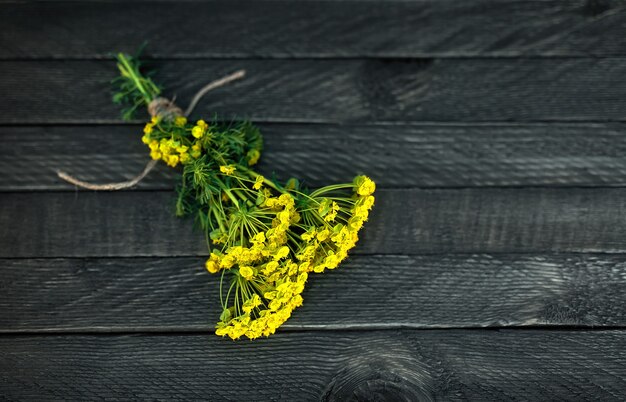 Ein kleiner Strauß wilder Blumen ist mit einem Seil gebunden und liegt auf einem hölzernen Hintergrund.