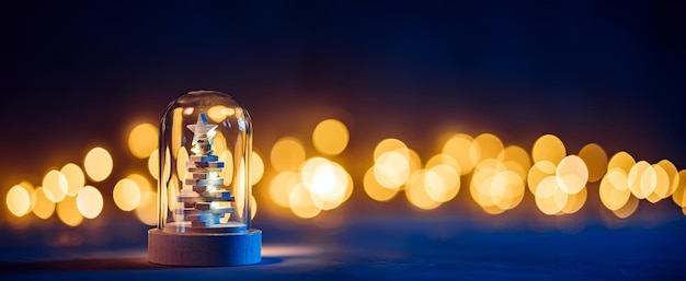 Ein kleiner Weihnachtsbaum aus Holz in einer Glaskuppel in der Dunkelheit der Winternacht auf dem Hintergrund von Bokeh-Lichtern