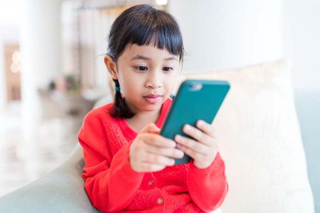 Ein kleines asiatisches Mädchen spielt zu Hause mit dem Handy.
