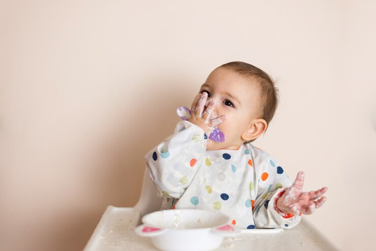 Ein kleines Baby, das ihr Abendessen isst und ein Durcheinander mit Joghurt und Getreide macht