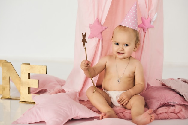 Ein kleines Baby in einem rosa Zelt mit einem Zauberstab in der Nähe eines großen Kuchens.