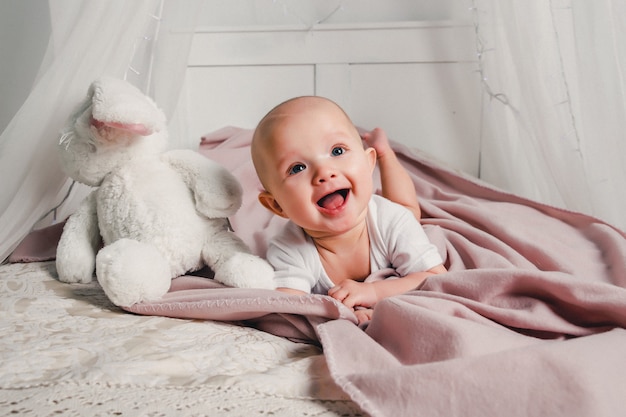 Ein kleines Baby liegt auf einem Bett mit einem Spielzeugkaninchen und lächelt