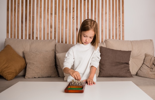 Ein kleines blondes Mädchen sitzt an einem Tisch und spielt Schach in einem Raum