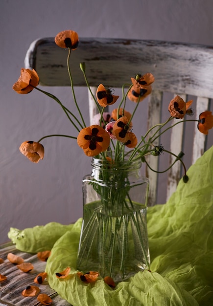 Ein kleines Bouquet aus roten Mohnblumen im klassischen Stil Stillife von Popies in einer Brillenvase auf Vintage