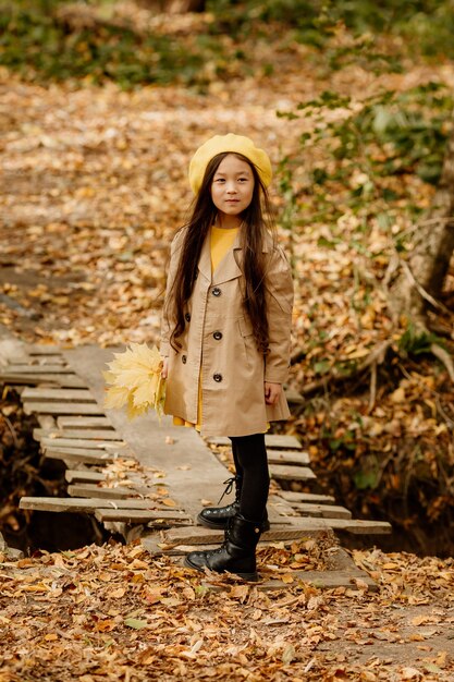 Ein kleines brünettes asiatisches Mädchen in Herbstkleidung geht im Herbstwald in der Nähe eines Baches