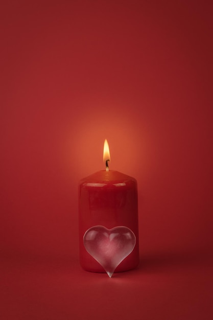 Ein kleines Glasherz und eine brennende rote Kerze auf rotem Grund. Das Konzept einer romantischen Beziehung.