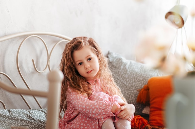 Ein kleines grüblerisches Mädchen sitzt auf einem Bett im Kinderzimmer. Kinderträume. Glückliche Kindheit