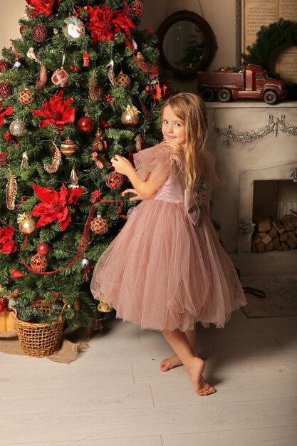 ein kleines hübsches blondes Mädchen in einem rosa Kleid schmückt den Weihnachtsbaum