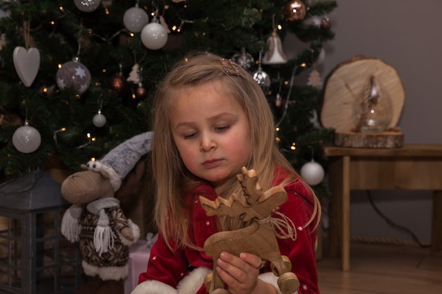 Ein kleines hübsches Mädchen mit Weihnachtsgeschenken sitzt am Weihnachtsbaum im Zimmer, Neujahrskonzept