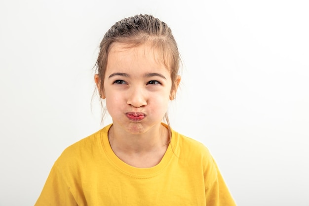 Ein kleines kaukasisches Mädchen macht lustige Gesichter auf einem weißen Hintergrund, isoliert