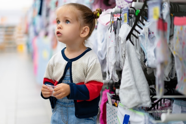 Foto ein kleines kaukasisches mädchen steht nahe einem schaufenster mit kleidung und unterwäsche in einem großen speicher.