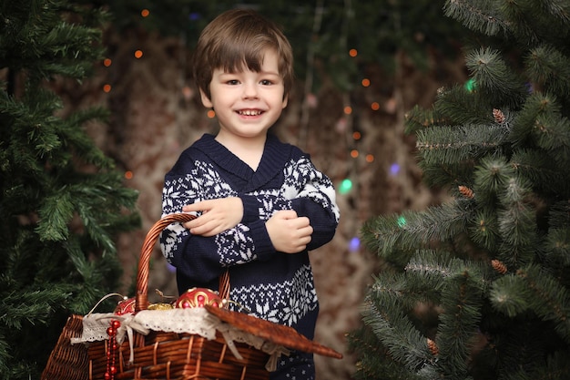 Ein kleines Kind am Neujahrsbaum. Kinder schmücken den Weihnachtsbaum. Baby in einem Pullover von einem grünen Baum im Studio.