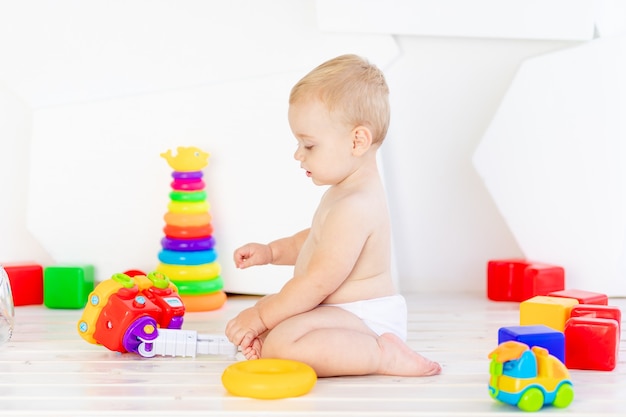 Ein kleines Kind, ein Junge spielt mit hellen Spielsachen in einem hellen weißen Raum in Windeln