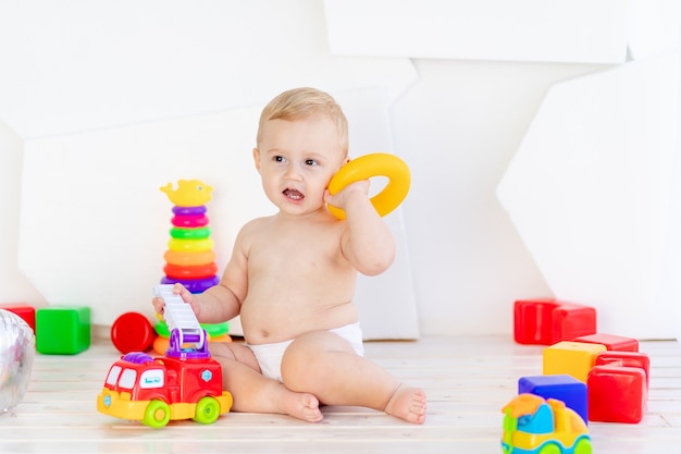 Ein kleines Kind, ein sechs Monate alter Junge, spielt mit hellen Spielsachen in einem hellen weißen Raum in Windeln