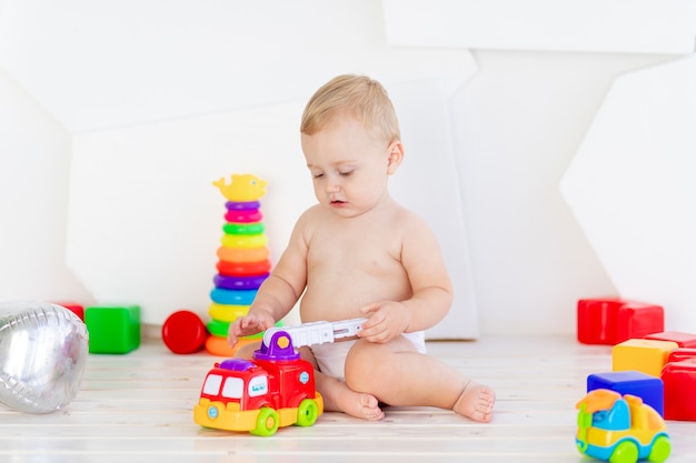 Ein kleines Kind, ein sechs Monate alter Junge, spielt mit hellen Spielsachen in einem hellen weißen Raum in Windeln