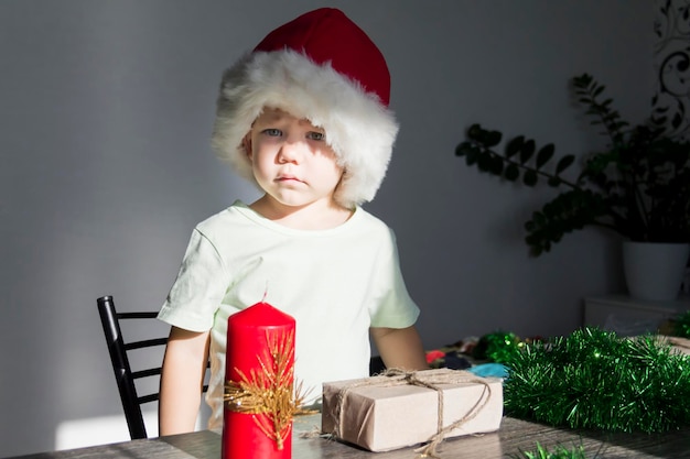 Ein kleines Kind in einem Weihnachtsmann-Hut mit Geschenken am Neujahrstisch