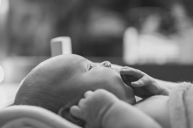 Ein kleines Kind liegt auf einem Holzbett unter einer Decke. Baby saugt Finger. Konzept der Kindheit, Gesundheit und In f, Kindermöbel, Interieur, Holzprodukte