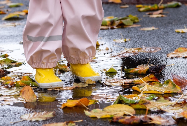 Ein kleines Kind mit gelben Stiefeln spritzt in eine Regenpfütze mit Herbstlaub