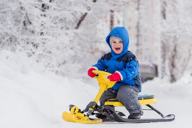 Ein kleines Kind sitzt im Winter auf einem Schneeroller