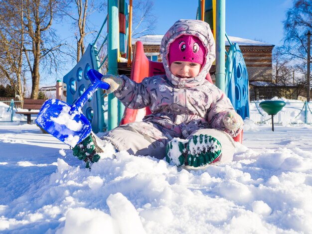 Ein kleines Kind spielt auf dem Spielplatz mit Schnee.