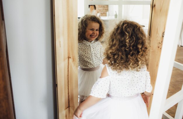 Ein kleines lockiges Mädchen betrachtet sich im Spiegel und lacht. Kinderglück Freude