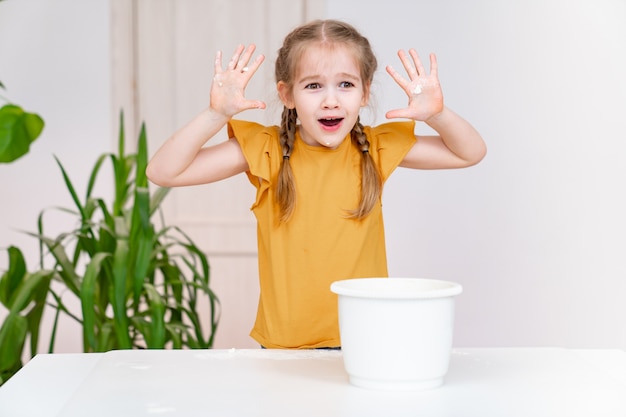 Ein kleines lustiges Mädchen zeigt mit Mehl beschmierte Hände