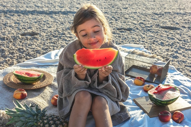 Ein kleines Mädchen an einem Sandstrand isst eine Wassermelone