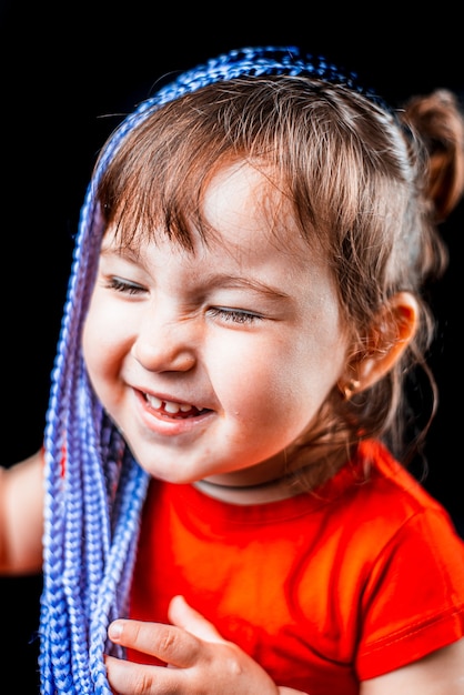 Ein kleines Mädchen auf einem schwarzen Hintergrund mit Afro-Zöpfen, künstlich in Gummibändern geflochten und süß angezogen
