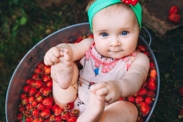 Ein kleines Mädchen badet in einem Becken mit Erdbeeren im Garten.