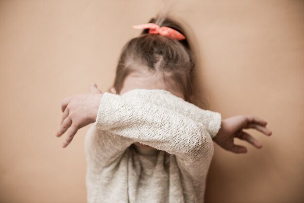 Ein kleines Mädchen bedeckt ihr Gesicht mit den Händen. Selektiver Fokus