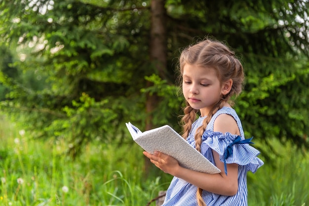 Ein kleines Mädchen, das ein Buch in einem grünen Park liest