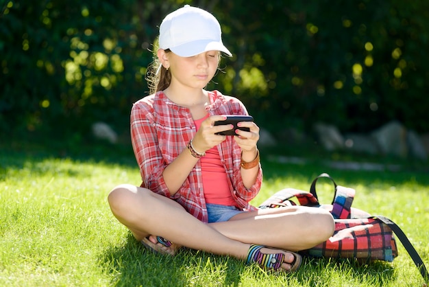 Ein kleines mädchen, das im gras spielt mit einem telefon sitzt