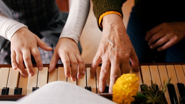 Ein kleines Mädchen, das im Musikunterricht Klavier spielt, hilft einer Lehrerin, ihre Hände zu schließen