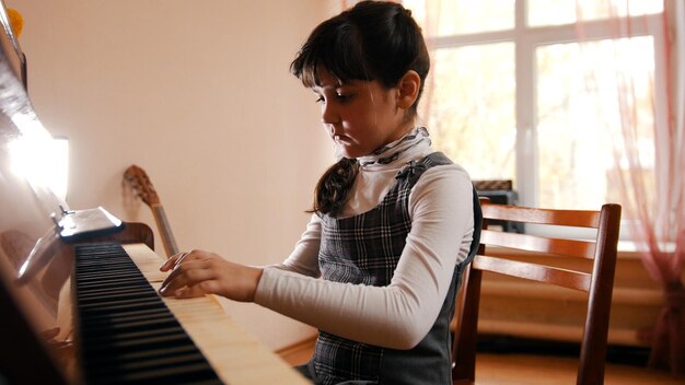 Ein kleines Mädchen, das im Musikunterricht Klavier spielt, schöne Sonnenlichthände auf den Tasten