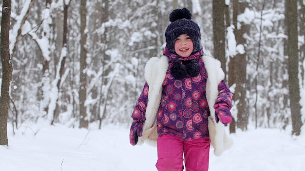 Ein kleines Mädchen, das im Winterwald mit Schnee spielt