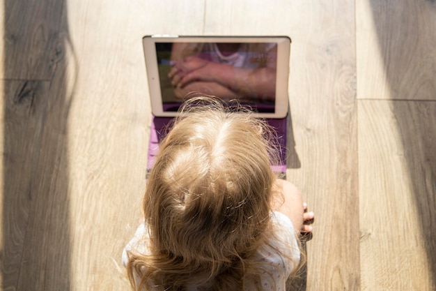 Foto ein kleines mädchen, ein kind, das auf dem boden liegt, schaut auf das tablet, das oben flach liegt.