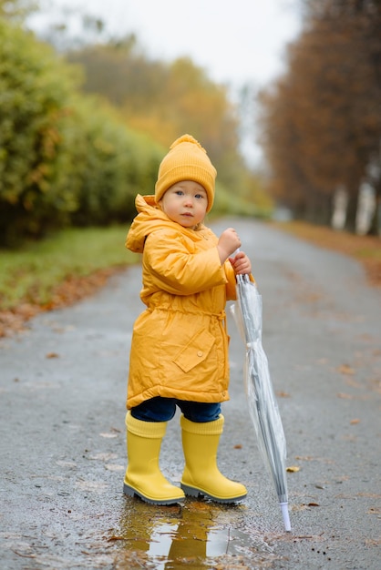 Ein kleines Mädchen geht mit einem Regenschirm in gelben Gummistiefeln und einem wasserdichten Regenmantel Autumn Walk