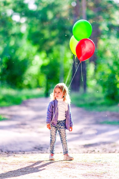 Ein kleines Mädchen hält die Ballons im Wald vor dem Hintergrund grüner Bäume in den Händen