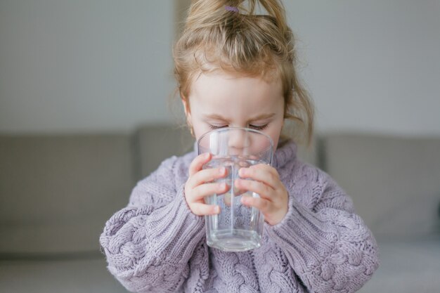 Ein kleines Mädchen hält ein Glas Wasser und trinkt. Gemütlich.