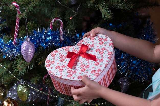 Ein kleines Mädchen hält ein großes Neujahrsgeschenk und ein Geschenk auf dem Hintergrund eines Weihnachtsbaums